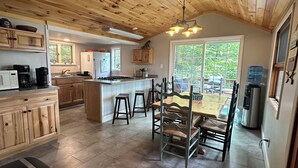 A spacious kitchen with wooden cabinets, a central island, and a dining area with a table and chairs. - The Sauna Cottage on Keuka Lake - Wine Trail Retreat (Keuka Park)