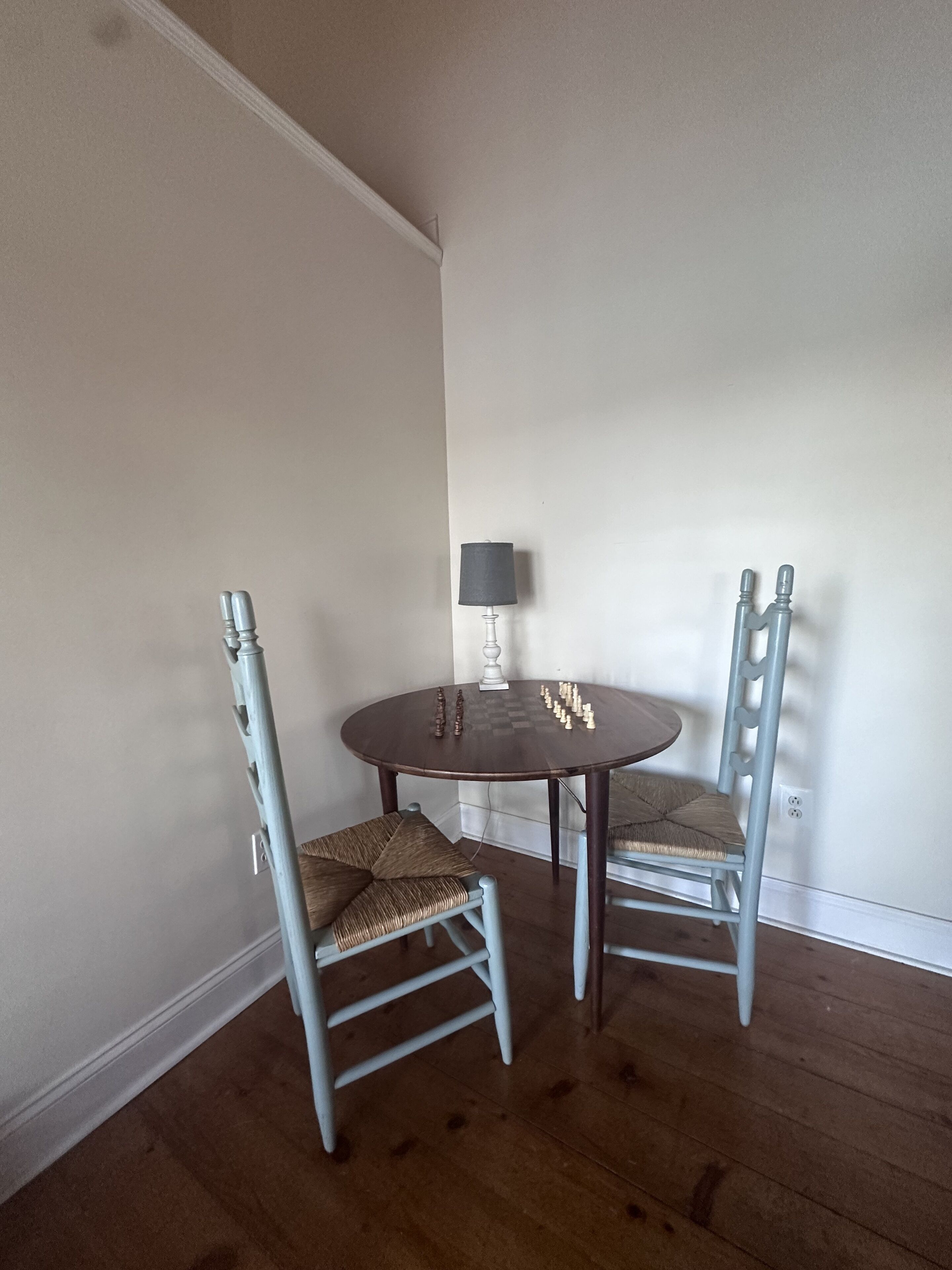 A dining area with a round table and two chairs, a lamp, and a wall socket.