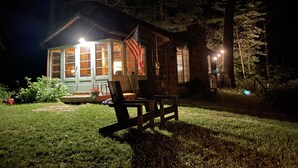 A cabin with a large window, a porch with a chair, and a small table. - The Sauna Cottage on Keuka Lake - Wine Trail Retreat (Keuka Park)