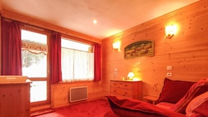 A cozy room with a bed, a dresser, a window with curtains, a radiator, and a wall-mounted lamp.