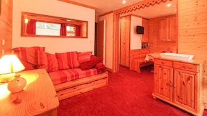 A cozy room with a wooden sofa, a small table with a lamp, a wooden cabinet, and a window with curtains.