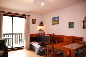 Un salon confortable avec un canapé, une table à manger et des chaises. Une porte-fenêtre coulissante donne accès à un espace extérieur.