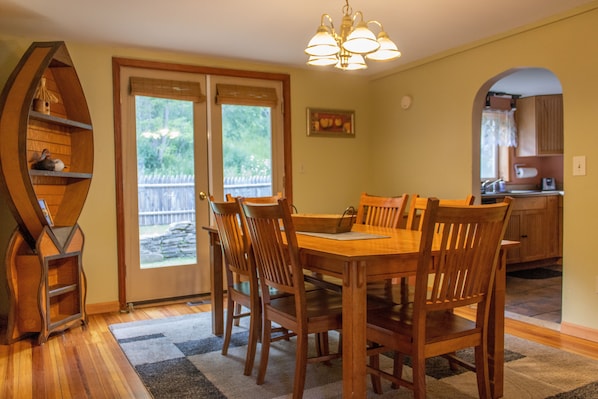 A dining area with a wooden table and chairs, a chandelier, and a view of the backyard through glass doors. - Cozy Cottage On The Susquehanna River (Portlandville)