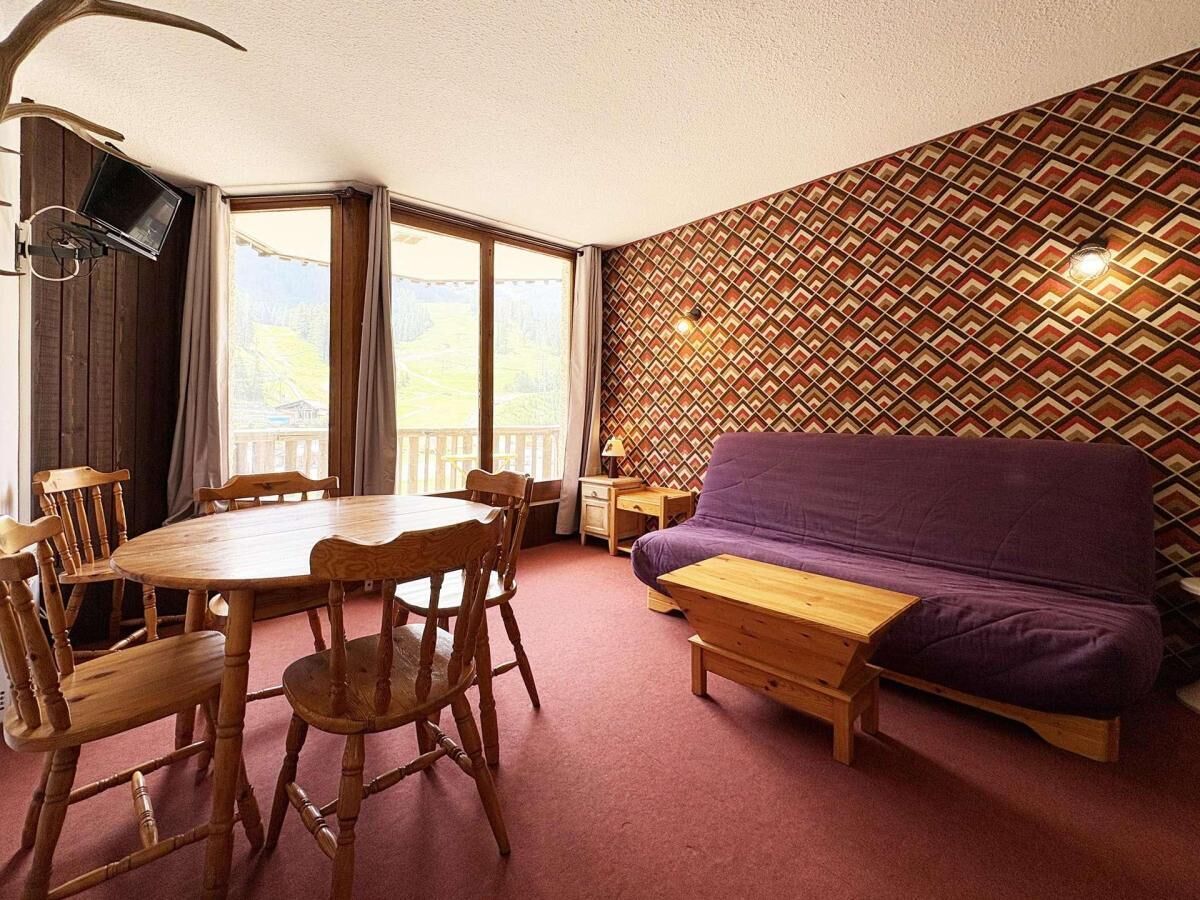 A room with a round wooden table, four chairs, a purple sofa, and a patterned wall.