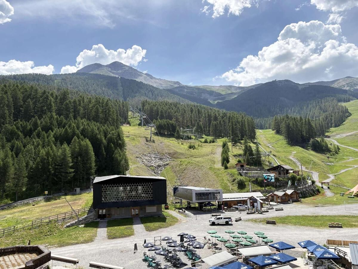 Eine gebirgige Landschaft mit einem Skigebiet, einschließlich eines Hotels, einem Parkplatz und Sitzgelegenheiten im Freien.