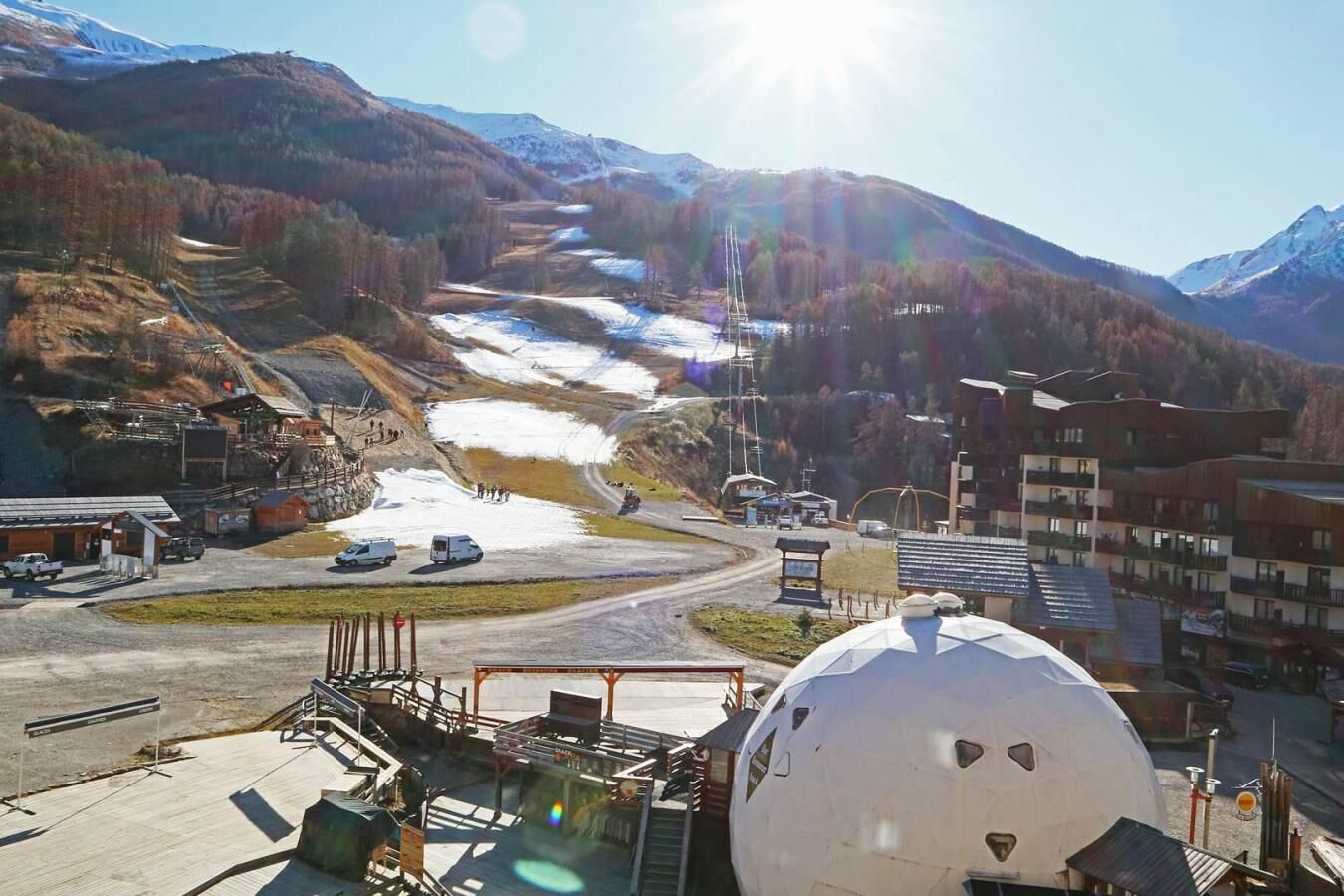 Un paisaje montañoso con un complejo turístico de esquí, que incluye una gran estructura en forma de cúpula, edificios y una carretera con vehículos.