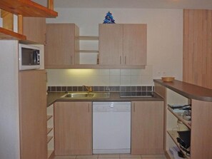 A compact kitchen with wooden cabinets, a microwave, a dishwasher, and a small sink.