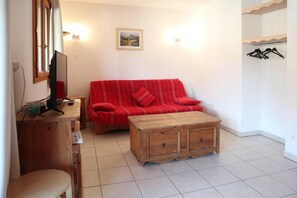 Et værelse med en rød sofa, et træ sofabord, et skrivebord med en computer og et billede på væggen.