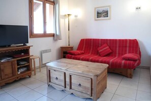 A living room with a red sofa, a wooden coffee table, a TV on a wooden stand, a floor lamp, and a radiator.