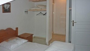 Un dormitorio con cama, mesita de noche de madera, armario y una puerta que da a otra habitación.