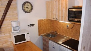Una cuina compacta amb microones, torradora, rentapelats i un rellotge a la paret.