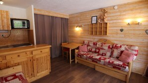 Interior acollidor d'una cabana amb una cuina de bar petitesa de fusta, un sofà amb funda de retalls i una taula de dinar.