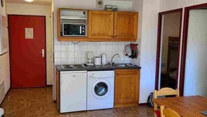 A compact kitchen with wooden cabinets, a microwave, a washing machine, and a dining area with a table and chairs. - 150m from ski slopes, 4th floor, view mountain, balcony, parking, ski locker, 36m², Valfréjus (Valfréjus)