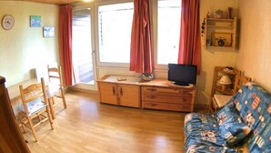 Una habitación acogedora con techo de madera, un sofá, un televisor sobre un mueble de madera, una mesa de comedor con sillas y una ventana con cortinas.