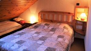 Une chambre confortable située sous les toits, avec deux lits simples, des têtes de lit en bois et une petite table de chevet avec une lampe.