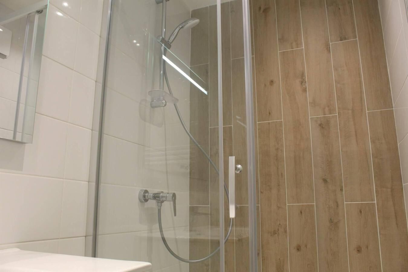 Un baño moderno con cabina de ducha de vidrio, azulejos blancos y suelo de madera.