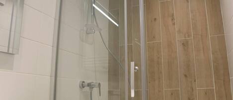 Un baño moderno con cabina de ducha de vidrio, azulejos blancos y suelo de madera.