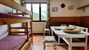 A room with bunk beds, a dining table with chairs, a radiator, and a window with a view of the outdoors. - 100m from ski slopes, 3rd floor, tv, 18m², Vars (Vars)