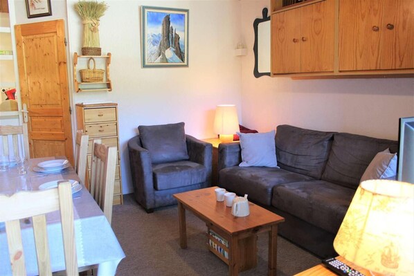 A cozy living room with a wooden dining table, two armchairs, a sofa, and a TV.