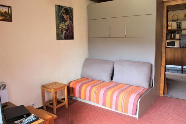 Una habitación compacta con sofá, una pequeña mesa de madera, televisión y zona de cocina con microondas.