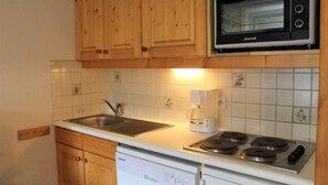 A kitchen with wooden cabinets, a stainless steel sink, a coffee maker, and a Brandt microwave. - 200m from ski slopes, Ground floor, terrace, tv, 42m², Vars (Vars)