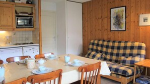 A cozy room with a dining table set for four, wooden chairs, a checkered sofa, a microwave, a refrigerator, and a painting on the wall. - 200m from ski slopes, Ground floor, terrace, tv, 42m², Vars (Vars)