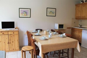 A dining area with a table set for four, wooden chairs, a television, a microwave, and wooden cabinets. - 50m from shops, Ground floor, terrace, tv, 42m², Vars (Vars)