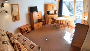A cozy room with a sofa, a small table, a TV, and a dining area with chairs.