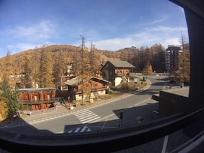 Vista de uma estrada com edifícios e uma colina arborizada ao fundo.