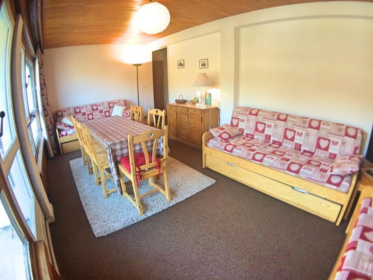 A cozy room with a wooden table and chairs, a sofa with patterned cushions, and a small cabinet.
