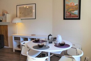 A dining area with a white table and chairs, a lamp, and a map and poster on the wall. - 50m from resort center, 7th floor, view mountain, balcony, parking, tv, 28m², Vars (Vars)