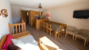 A compact living space with a kitchenette, a dining area, a TV mounted on the wall, and a bed with pillows.