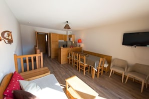Ein kompakter Wohnraum mit Küchenzeile, Essbereich, an der Wand befestigtem Fernseher und einem Bett mit Kissen.