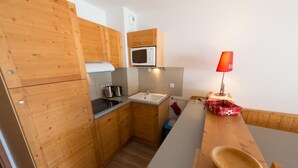 A compact kitchen with wooden cabinets, a microwave, a sink, and a red lamp.