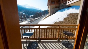 A balcony with two chairs and a table, overlooking a snowy mountain landscape and a road.
