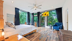 Un'ampia camera da letto con un grande letto, un tavolino in legno, una poltrona blu e una ventola a soffitto.
