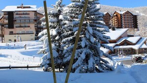 Ett snötäckt landskap med en stuga och ett stort, vintergrönt träd i förgrunden.