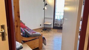 Ett litet, ombonat rum med en säng, ett skrivbord, en stol, en golvlampa och ett fönster med gardiner.