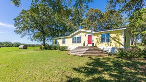 A yellow house with a red door, surrounded by a grassy yard and trees. - Rural Retreat with Private Pond, ATV Trails and Event Space (Buffalo)