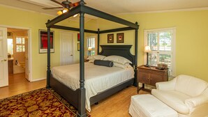 A four-poster bed with a dark frame, a wooden nightstand with a lamp, and a white armchair. - Rural Retreat with Private Pond, ATV Trails and Event Space (Buffalo)