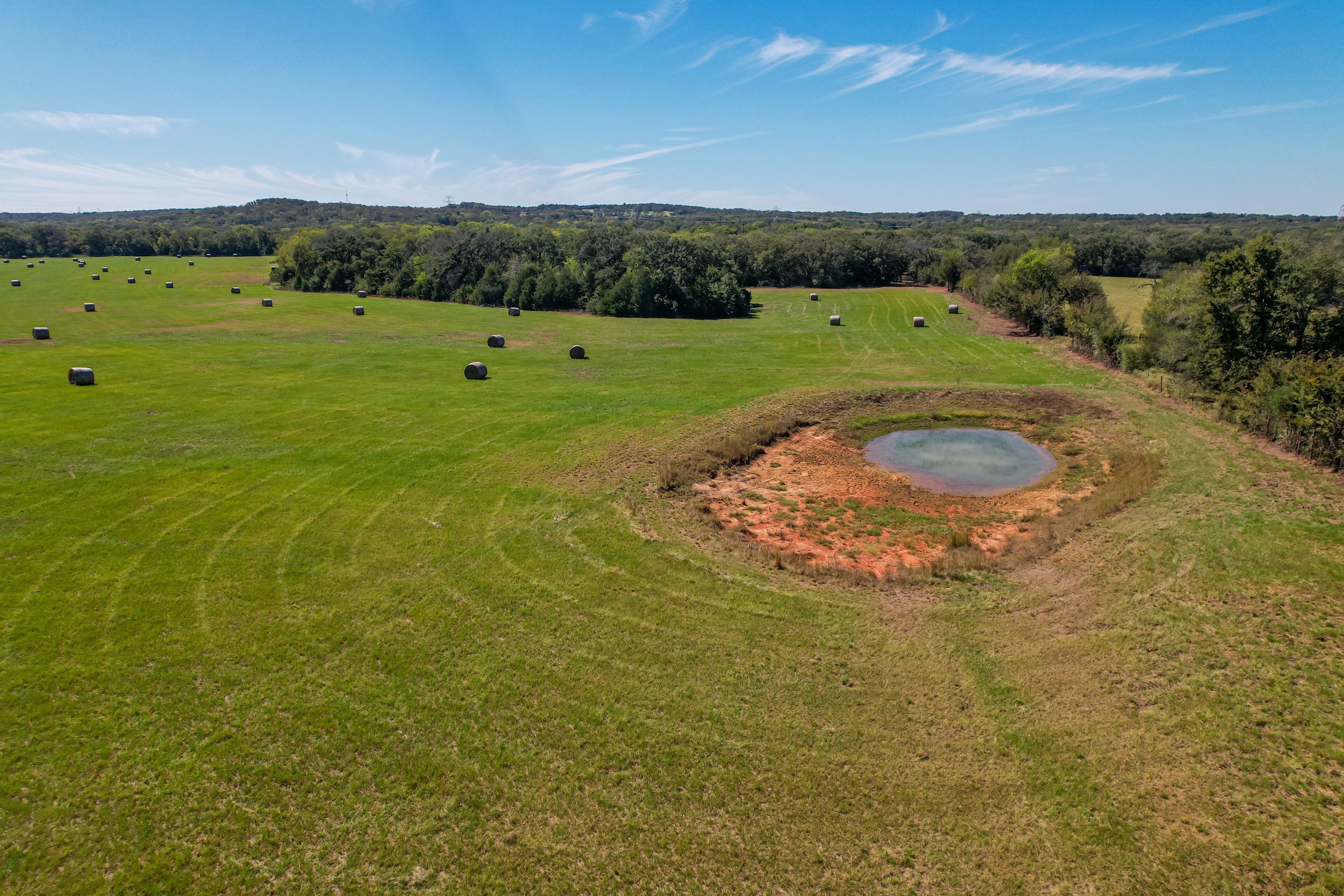 A large open field with hay bales and a circular pit.