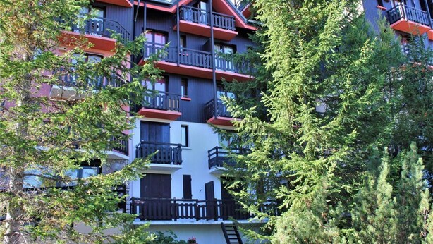 Un immeuble à plusieurs étages doté de balcons, entouré d’arbres.