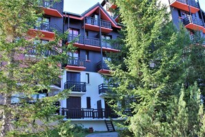 Un edificio de varios pisos con balcones, rodeado de árboles.