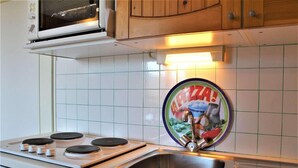 Une cuisine équipée d’une cuisinière, d’un four à micro-ondes et d’un évier. Un mur est décoré sur le thème de la pizza.