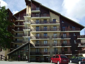 A multi-story hotel with balconies on each floor, a glass entrance, and cars parked in front.