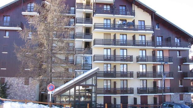 Un edificio de varios pisos con balcones, un telesilla y un cartel de prohibido estacionar.