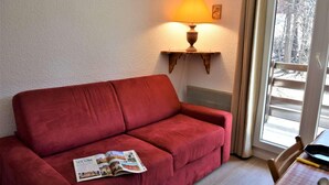 Un sofá rojo con una revista, una mesa con una cuchara y una lámpara en la pared.