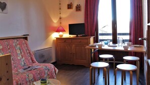 A cozy room with a bed, a TV, a table with chairs, and a window with curtains. - 50m from ski slopes, 3rd floor, balcony, tv, ski locker, 24m², Risoul (Risoul)