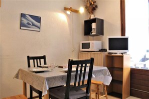 Un coin repas avec une table dressée pour deux personnes, un four à micro-ondes, une télévision et une petite étagère sur laquelle est posé un vase.
