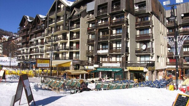 Un hôtel à plusieurs étages doté de balcons, avec une piste de ski en premier plan et divers commerces.